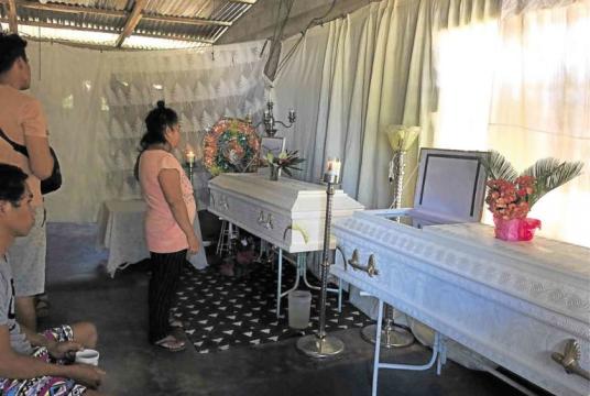 Leonora Avelino stands before the coffins of her husband, Ismael, and brother-in-law, Edgardo, who were slain by officers in a military-backed police operation in Canlaon City, Negros Oriental province, early on Saturday. —CONTRIBUTED PHOTO