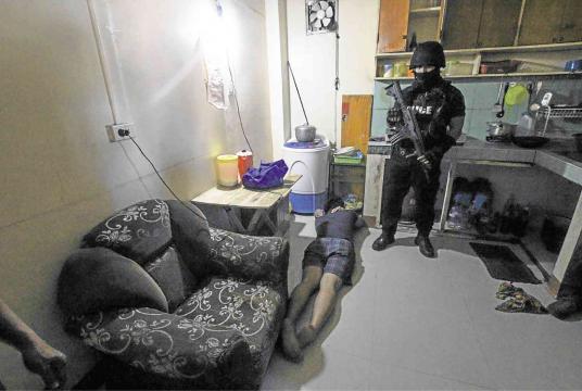 An officer from the Special Weapons and Tactics force of the Manila police watches a suspect captured during a drug raid on a house on Maliwanag Street in San Miguel, Manila, near Malacañang on Thursday. Police killed another suspect and seized “shabu” (crystal meth) worth P3 million during the operation. -EARVIN PERIAS