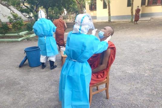 A healthcare staff is performing a swab test over a monk (Photo-Maha Warazein Masoeyein Damha Sarira School)