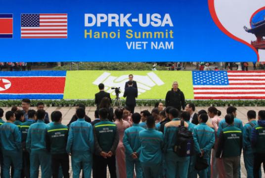 Vietnamese officials stand facing a sign installed for the US-North Korea summit in Hanoi on Sunday (Yonnhap)