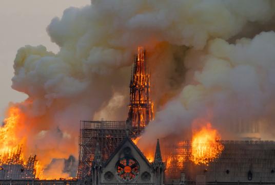 Smoke billows as flames burn through the roof of the Notre-Dame de Paris Cathedral on April 15, 2019, in the French capital Paris. - A huge fire swept through the roof of the famed Notre-Dame Cathedral in central Paris on April 15, 2019, sending flames and huge clouds of grey smoke billowing into the sky. The flames and smoke plumed from the spire and roof of the gothic cathedral, visited by millions of people a year. A spokesman for the cathedral told AFP that the wooden structure supporting the roof was b