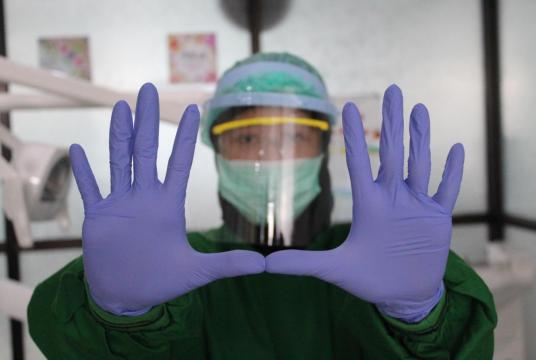 A health worker holds up gloved hands on March 27, 2020. Health workers are facing a shortage of medical gloves and other protective gear amid the coronavirus outbreak. JP/Fauzan (JP/Fauzan) 