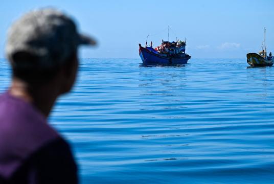 A man on a vessel looks at Rohingya refugees on a boat anchored off the coast of Labuhan Haji in Southern Aceh province on October 22, 2024. (AFP/Chaideer Mahyuddin)