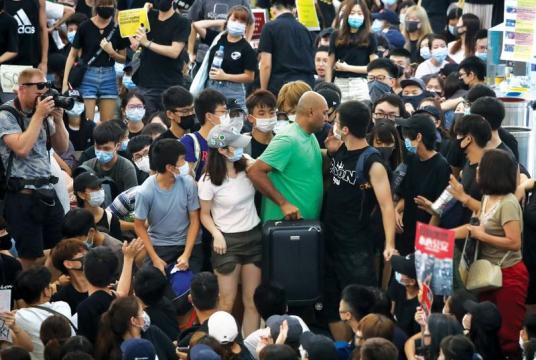 An airline passenger, wearing a green shirt, works his way to a gate of the departure hall through the jam-packed Terminal 1 at Hong Kong International Airport on Tuesday. For the second straight day, the aviation hub came to a virtual standstill as thousands of protesters swarmed the facility to extend their sit-in. (PHOTO / CHINA DAILY)