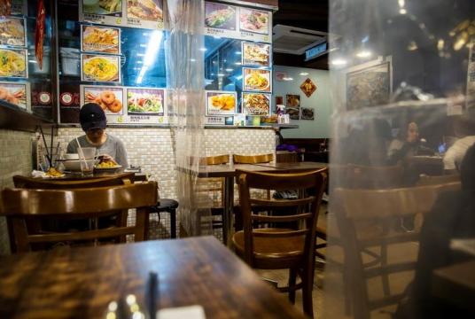 A customer (left) sits in a restaurant where sheets of plastic hang down from above to make sure people adhere to social distancing in Hong Kong on March 29, 2020. (ISAAC LAWRENCE / AFP)