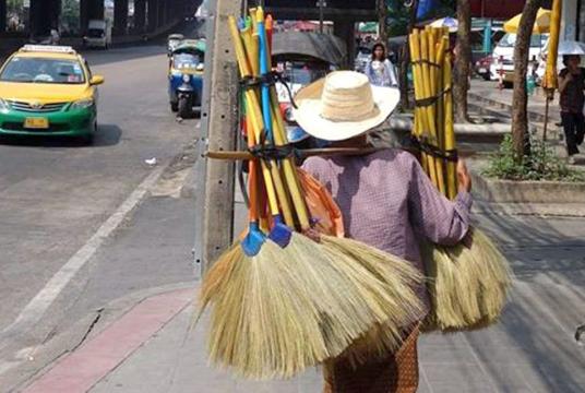 An elderly woman carries broomsticks as she hopes to sell them for a living on a Bangkok street. She is among millions of Thais who get old before accumulating enough savings for a comfortable retirement life./The Nation