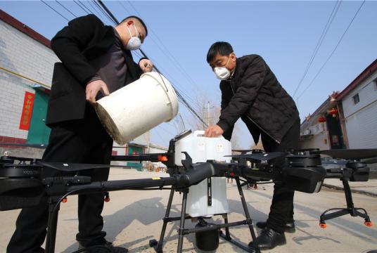 Workers pour disinfectant into a drone's tank in Zhengwan village, Handan, Hebei province, on Jan 31. The drone is used to spray disinfectant on roads in the village. [Photo by Hu Gaolei/For China Daily] 