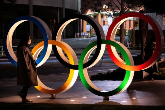 A woman wearing a protective face mask, following the outbreak of the coronavirus, walks past The Olympic rings in front of the Japan Olympics Museum in Tokyo, Japan, March 3, 2020. [Photo/Agencies] 