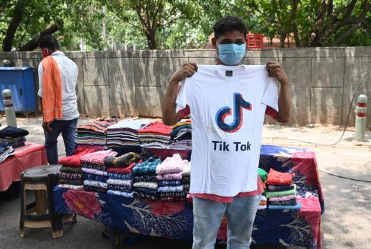 A vendor poses in front of his stall with a T-shirt bearing the logo of the video-sharing application TikTok in New Delhi on Tuesday, June 30, 2020. The Indian government announced a decision on Monday to block 59 Chinese apps citing "sovereignty and integrity" concerns. [Photo/Agencies]