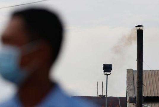 A man wears a mask as smoke is released from a factory chimney behind him in Phnom Penh in 2017. The Ministry of Environment will begin keeping tabs the city’s air quality with a PM2.5 monitor. Hong Menea/Phnom Penh Post
