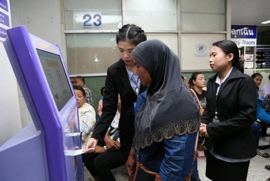 Trang Hospital staff members help a visitor print out a queue card from a “smart kiosk”.