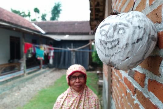 Yasmini, who lives in Wajak Kidul village in Tulungagung, East Java, looks at a 'tetek melek' mask fastened on the outer wall of her home. Some villagers have been placing the masks around their houses to "ward off" COVID-19. (JP /Asip Hasani)