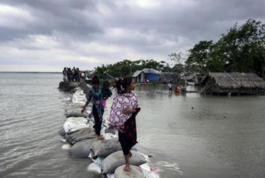 Children walk over the top of a sandbag embankment that was breached by high waters in Khulna on May 4, 2019, after Cyclone Fani reached Bangladesh. Photo: AFP/File