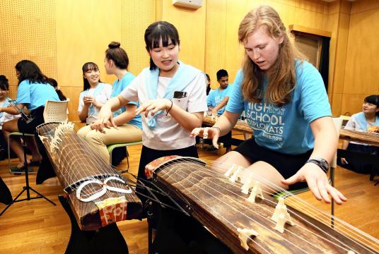 A Japanese student teaches a foreign exchange student on how to play a traditional Japanese musical instrument.