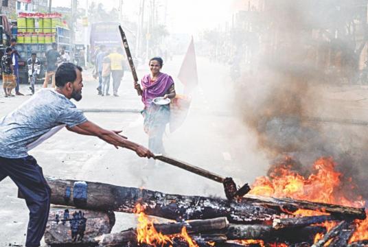 A jute mill worker sets fire to a stack of logs while another looks on during a blockade in Khulna’s Notun Rasta Mor on the Dhaka-Khulna highway yesterday. Jute workers continued their protests for the eight consecutive day demanding arrears. Photo: Star