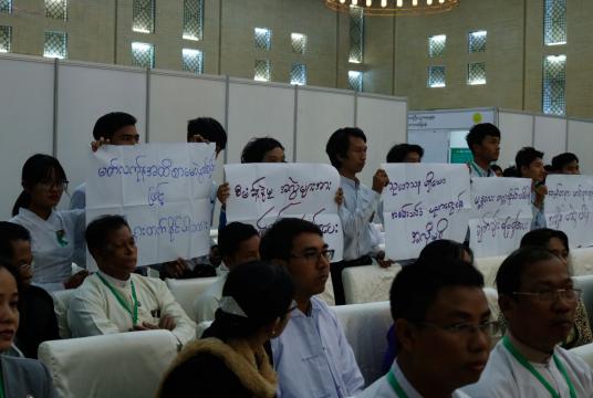 Students hold placards in their protest while State Counsellor is making a speech 