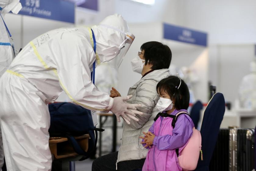 A staff member teaches a woman and a girl how to disinfect their hands while waiting to be registered at the new transit hub venue in the China International Exhibition Center in Beijing, on March 25, 2020. [Photo by Zou Hong/chinadaily.com.cn]
