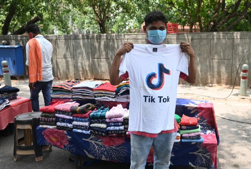 A vendor poses in front of his stall with a T-shirt bearing the logo of the video-sharing application TikTok in New Delhi on Tuesday, June 30, 2020. The Indian government announced a decision on Monday to block 59 Chinese apps citing "sovereignty and integrity" concerns. [Photo/Agencies]
