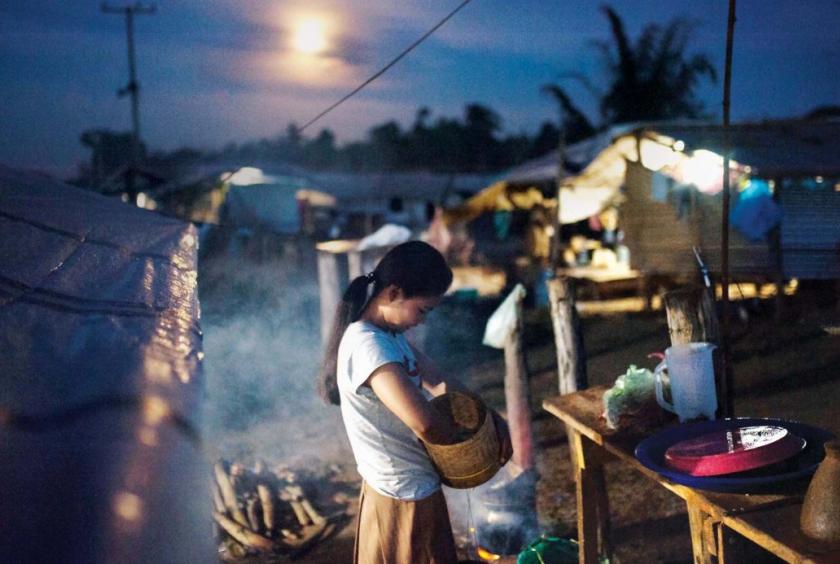 Six months after her home was washed away in the collapse of the dam, a woman cooks dinner behind her tent in Pindong camp. // Visarut Sankham