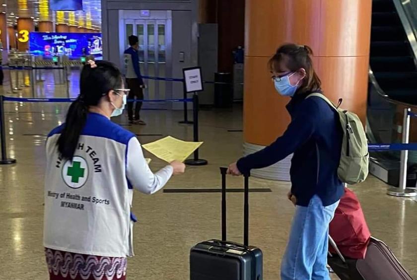 A health staff distributes leaflet on the prevention and control of the novel coronavirus to a passenger at Yangon International Airport.