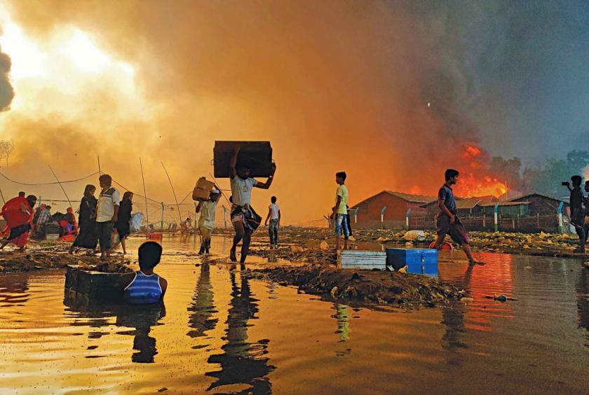 Refugees try to save whatever belongings they can as a fire rages through the Balukhali Rohingya refugee camp in Cox’s Bazar’s Ukhiya yesterday afternoon turning the entire sky orange. Many refugees in the tightly packed camp got injured trying to save their belongings and trying to get to safety. Photo: Courtesy of Ro Yassin Abdumonab