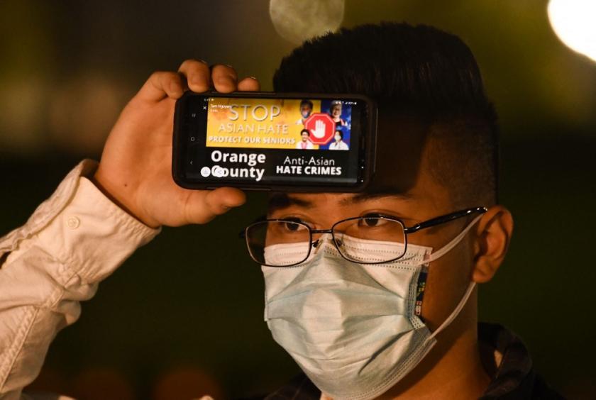 A person holds a phone with a message about hate crimes against Asian Americans during a vigil organized by Nailing It For America for those who have died from Covid-19 and to (AFP/PATRICK T. FALLON ) 
