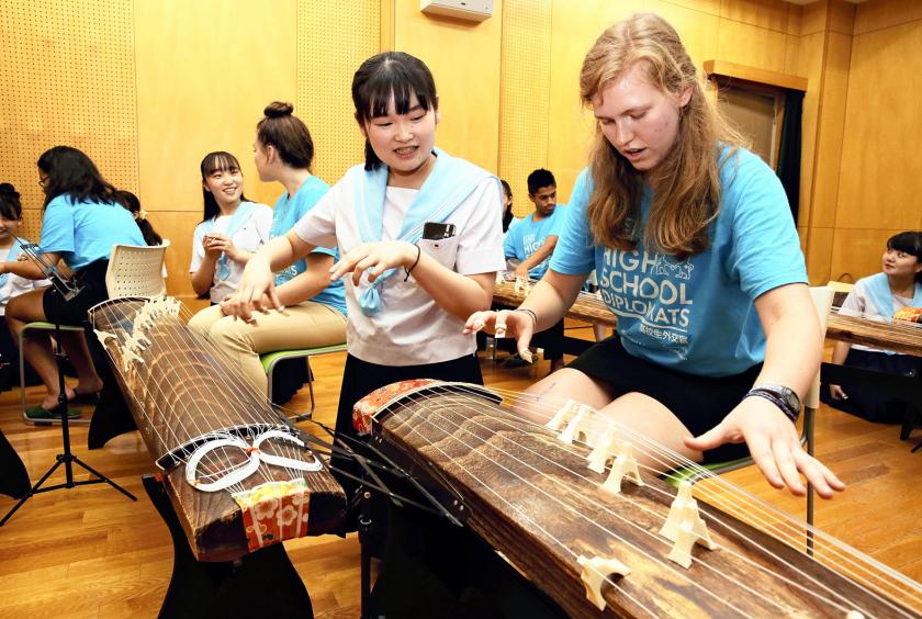 A Japanese student teaches a foreign exchange student on how to play a traditional Japanese musical instrument.