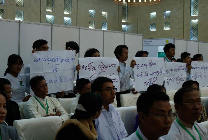 Students hold placards in their protest while State Counsellor is making a speech 