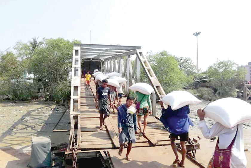 The workers carry rice bags to unload from the vessel.