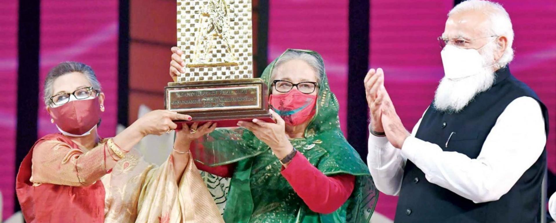 Prime Minister Sheikh Hasina and her younger sister Sheikh Rehana hold high the Gandhi Peace Prize-2020 awarded to Bangabandhu Sheikh Mujibur Rahman posthumously by the Indian government. Indian Prime Minister Narendra Modi is seen applauding next to them. Photo: PID